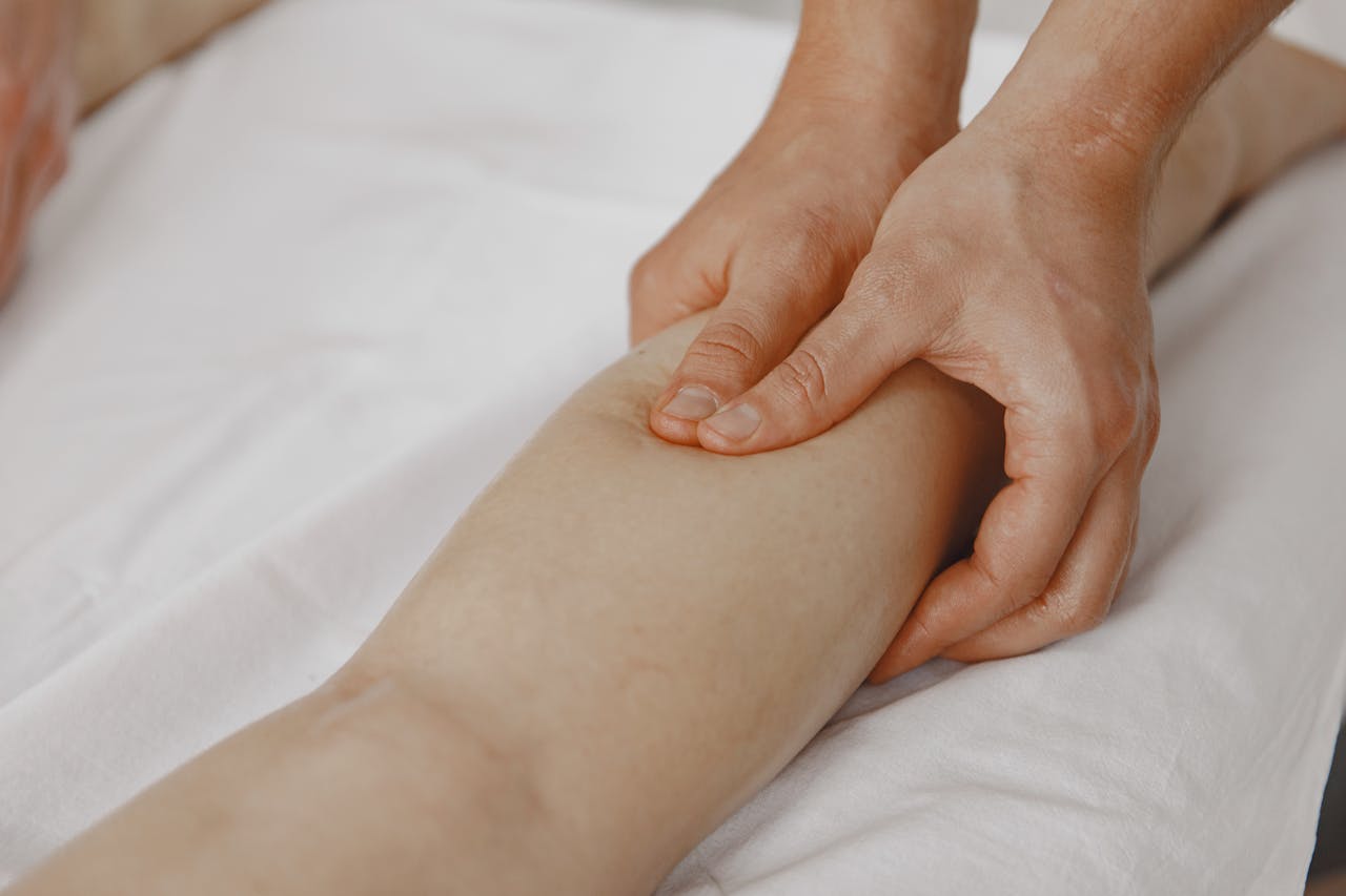 Home Close-up image of a massage therapist applying pressure on a client's leg for muscle relaxation.